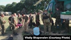 Поранені, зокрема цивільна жінка, готуються летіти з польового шпиталю до стаціонарних медичних закладів. Літо 2014 року
