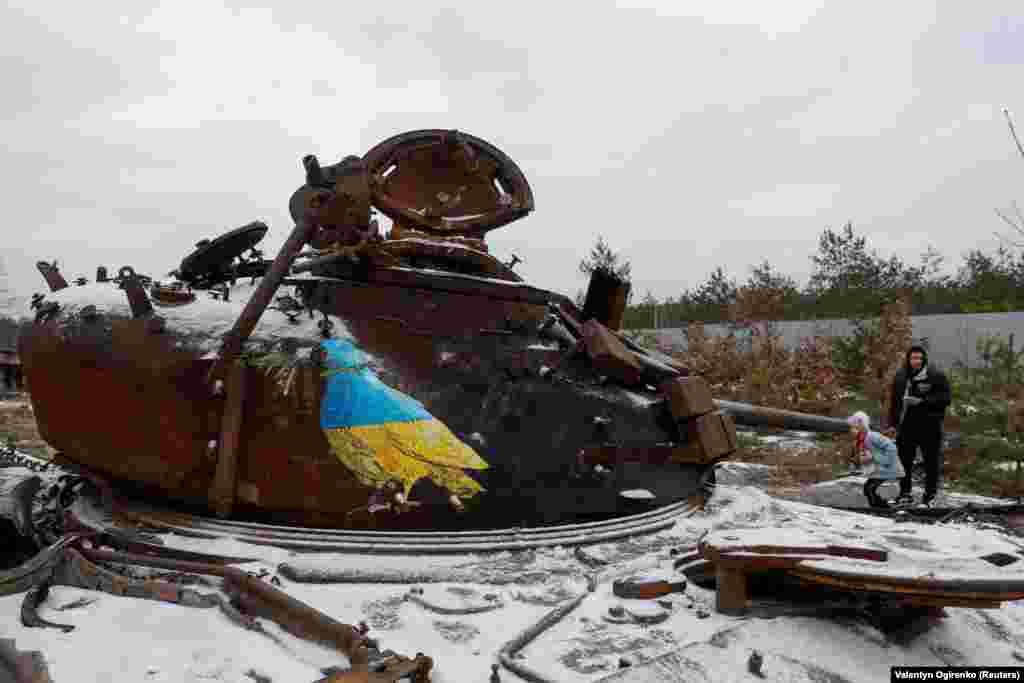 Люди стоять біля знищеного російського танка, на якому відомий вуличний художник Tvboy намалював ще одного голуба миру у кольорах українського прапора. Дмитрівка, Київщина, 29 січня 2023 року.