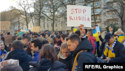 Люди тримали прапори ЄС та України, а також плакати англійською, українською та російською мовами з написами «Зупиніть війну» та «Україна = Європа»