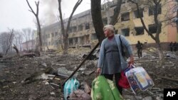 یوه ښځه په ماریوپول کې په برید کې له زیانمن شوي زېږنتون سره نېږدې ولاړه ده او له سیمې څخه د وتلو هڅه کوي - د مارچ ۱۰مې انځور.