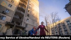 Жінка з дитиною виходять з пошкодженого авіаудром будинку у Києві, 16 березня 2022 року