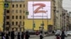 Pedestrians in St. Petersburg cross a street in front of a billboard supporting the Russian Army's unprovoked invasion of Ukraine. Displaying the letter Z in the colors of the ribbon of Saint George, it also contains a slogan saying: "We don't give up on our people."
