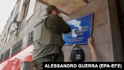 Російські військові змінюють табличку на міській раді окупованого українського Світлодарська. Травень 2022 року