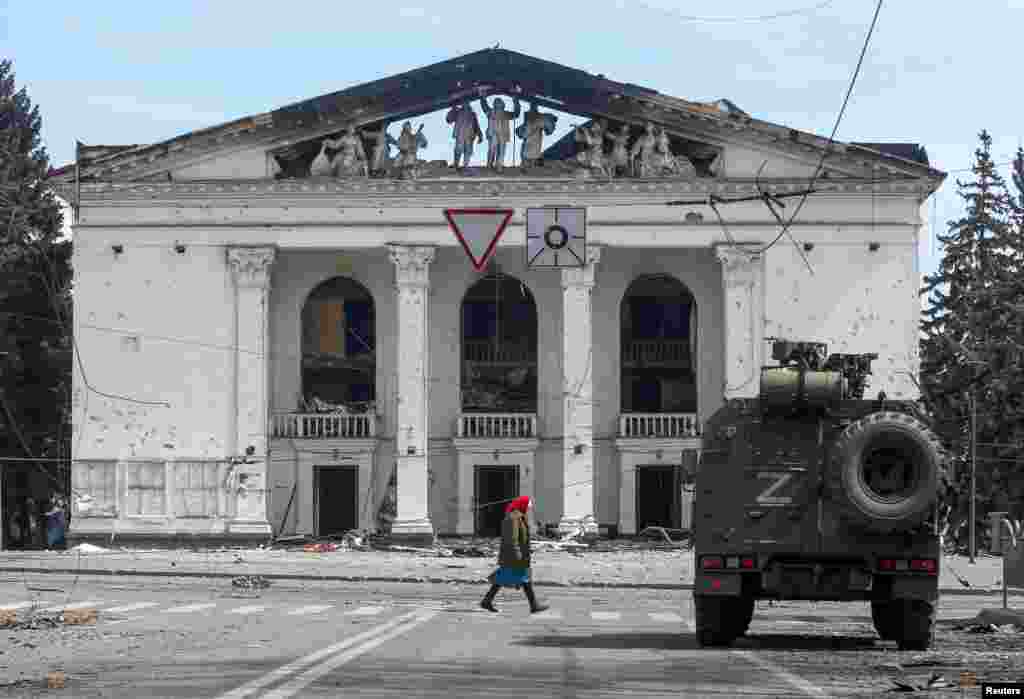 An elderly woman walks past the destroyed theater and an armored vehicle of pro-Russian forces in April 2022. 
