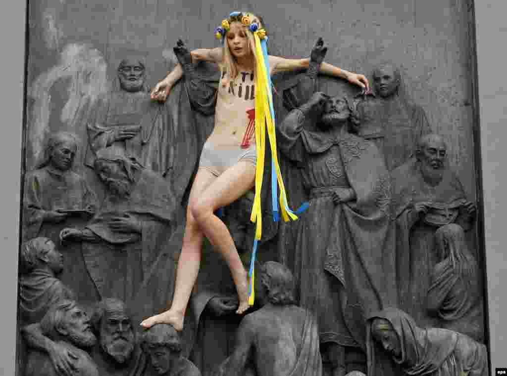 Активістка Femen Анна Алляйн вилізла на пам’ятник Київському князеві Володимиру із написом на грудях «Путін вбиває», Київ, 27 липня 2017 року. У заяві організації Femen зазначено, що цей жест символізує розп’яття. «Хода Московського патріархату вулицями Києва – це «тихий марш» кремлівського агресора, після якого можуть прийти танки», – наголошують у Femen. БІЛЬШЕ ПРО ЦЕ