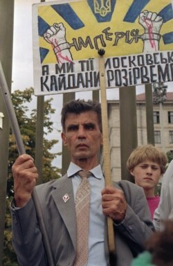 Чоловік тримає транспарант і прапор США в очікуванні на проїзд кортежу американського президента Джорджа Буша, який прибув із візитом до України. Київ, 3 серпня 1991 року