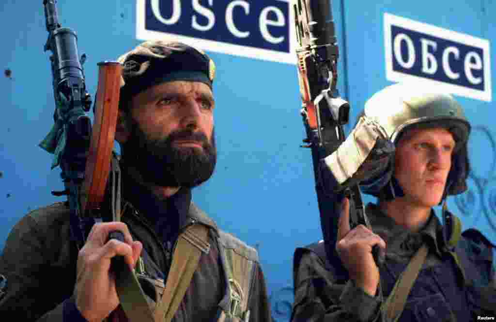 Чеченский и российский охранники наблюдают за толпой у здания, где проходят переговоры между российской делегацией и представителями Ичкерии 12 июля 1995 года в Грозном. Переговоры по семимесячному конфликту начались в прошлом месяце, но так и не смогли достичь соглашения по главному камню преткновения – будущему статусу Чечни