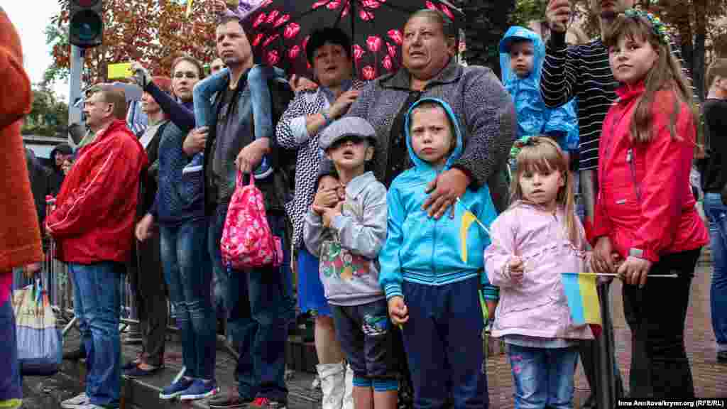 На бордюрах Крещатика собрались люди семьями, с друзьями или в одиночку они приветствовали шествие с цветами и украинской символикой 