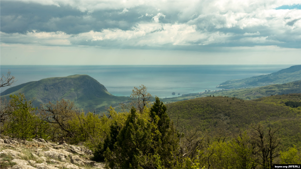 Вид с Парагильмена на горы Аю-Даг (слева) и Шарха (ближняя справа). На обратных, южных скатах, последней находится одноименный карьер. Он представляет собой систему горных выработок, вытянутых с юго-запада на северо-восток до 600 метров и шириной до 300 метров. Акционерному обществу «Шархинский карьер», как уже ранее сообщалось в некоторых медиа, почти на 100% принадлежит известный крымский застройщик «Консоль-Строй», внесенный в санкционный список США. К карьеру слева примыкает территория Алуштинского завода железобетонных конструкций