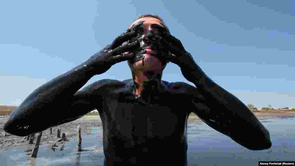 Отдыхающий намазывает себя лечебной грязью в водах озера Чокрак, что у села Курортное под Керчью