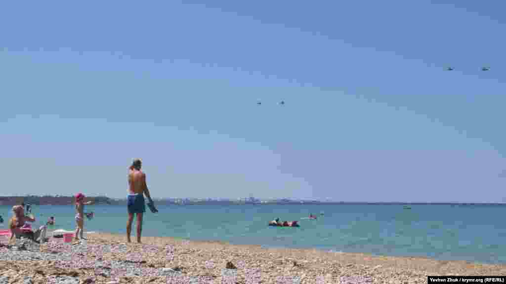 Пляжники наблюдают за российскими военными вертолетами. (Снимки сделаны незадолго до парада 26 июля, приуроченного ко Дню военно-морского флота в России. На фото – вертолеты возвращаются на базу после репетиции)