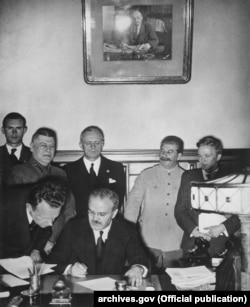 В’ячеслав Молотов у присутності Йосипа Сталіна та Йоахіма Ріббентропа підписує Договір про дружбу та кордони між СРСР та Німеччиною. Москва, Кремль, 23 серпня 1939 року