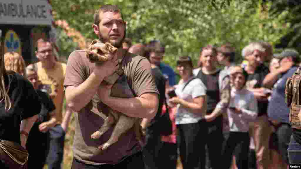 Muškarac nosi psa dok se stanovnici okupljaju blizu stambene zgrade koja je oštećena tokom ruskog raketnog napada na grad Dnipro u istočnoj Ukrajini.
