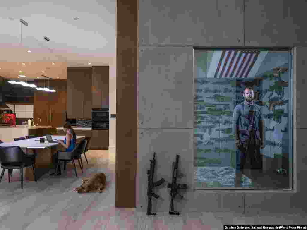 Ameriguns. Роберт Болдуін-молодший стоїть у своїй секретній збройовні за одностороннім дзеркалом у власному будинку в Лас-Вегасі, штат Невада, США, 16 квітня 2019 року. Його дівчина, Торі, сидить за столом. Роберт отримав свій перший пістолет – гвинтівку 22-го калібру – в подарунок від батька, коли йому було шість років.   Портрети: Перша премія, історії – Габріеле Галімберті для National Geographic