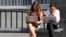 Young women work on laptops while waiting for a bus in Moscow.