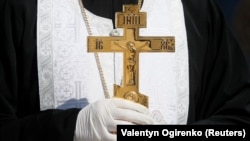 Священник Православної церкви України (ПЦУ) в захисних рукавицях (в час епідемії коронавірусу) під час освячення пасок для відправлення їх українським бійцям на лінію фронту. Київ, 13 квітня 2020 року 