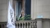 An official uses his smartphone next to the flag of the Islamic Emirate of Afghanistan at the balcony of the Afghan Embassy in Moscow on July 4.