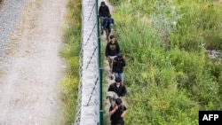 Migranți mergând de-a lungul unui gard de sârmă ghimpată la Dunkerque, în nordul Franței, pe 25 iunie 2025.