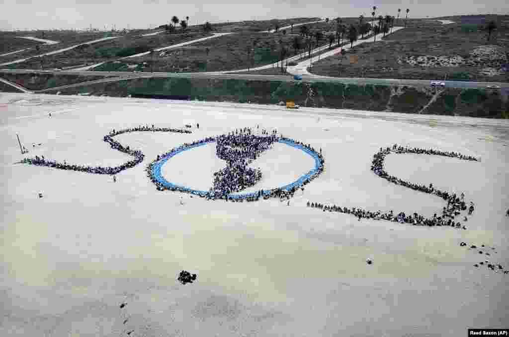 Близько 1500 школярів району Лос-Анджелеса сформували гігантське «SOS» із «O» у вигляді планети Земля з континентами Північної та Південної Америки, під час шостого щорічного проєкту прибирання на пляжі до Дня Землі, 22 квітня 1999 року