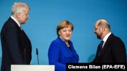 Прем’єр-міністр Баварії та глава Християнсько-соціального союзу Хорст Зігофер спотерігає за рукостисканням канцлера Анґели Меркель та лідера соціал-демократів Мартіна Шульца під час прес-конференції після чергового раунду коаліційних переговорів у січні 2018 року.