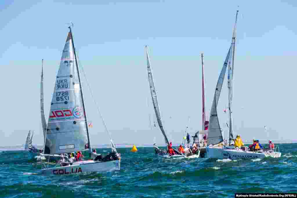 Яхти вишикуються біля стартової лінії поміж жовтих буйків – їм потрібно буде подолати дистанцію в приблизно дві морські милі