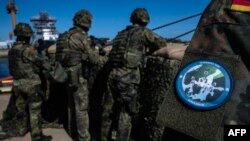 გერმანელი საზღვაო ქვეითი (მარჯვნივ) „კვადრიგას“ ემბლემით, ბუნდესვერის ნავსადგურის დაცვის ქვედანაყოფის გვერდით ვარნოუს გემთსაშენ ქარხანაში, როსტოკში, „კვადრიგა 2025-ის“ სამხედრო წვრთნების დროს. 4 სექტემბერი, 2025