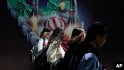 Iranian women without a mandatory head scarf, or hijab, walk past a banner in Tehran in April.