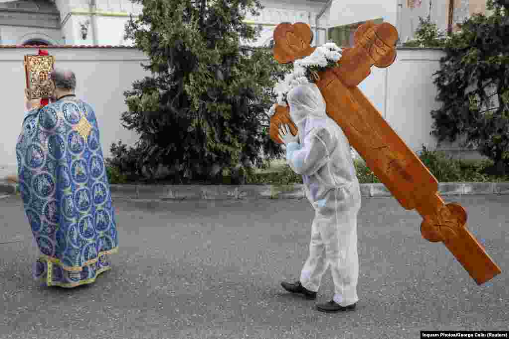 Волонтер в защитной одежде несет крест на религиозную службу в Бухаресте (Румыния) в Страстную пятницу, 17 апреля 