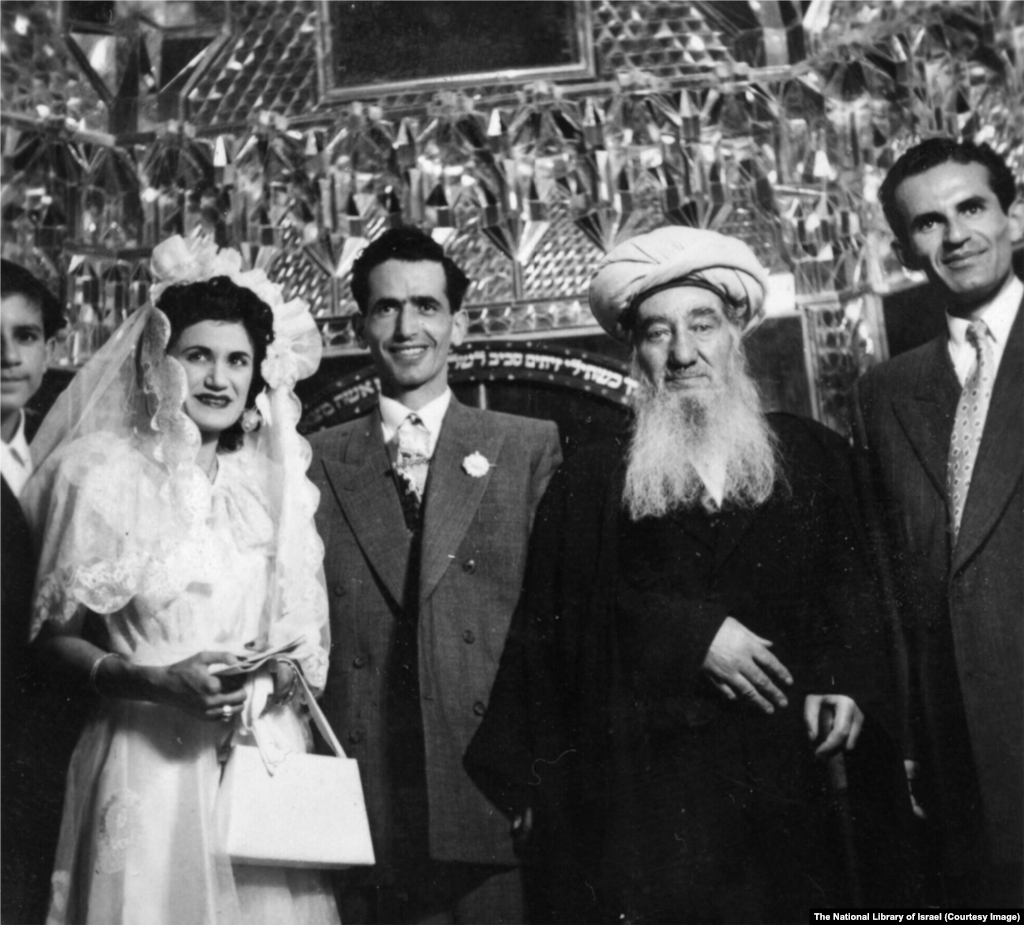 Еврейская свадьба в Иране в 1950-х годах. Церемонию проводит раввин Шломо Коэн Цедек (в центре справа), главный раввин страны.Надпись на иврите на заднем фоне — отсылка к Библии: «Жена твоя, как плодовитая лоза, в доме твоем; сыновья твои, как масличные ветви, вокруг трапезы твоей»