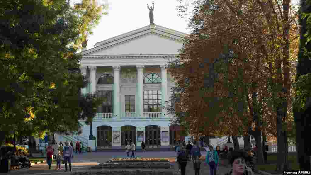 Лучи заходящего солнца «играют» на пожелтевших осенних листьях. Люди неспешно прогуливаются у Севастопольского академического русского драматического театра имени Луначарского