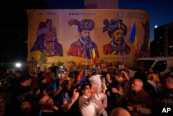 Сторонники Джордже Симиона реагируют на результаты экзитполов на фоне изображений румынских исторических фигур у штаб-квартиры Альянса за объединение румын (AUR) после закрытия избирательных участков в первом туре повторных президентских выборов в Бухаресте, 4 мая 2025 года