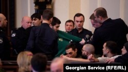 პენიტენციური სამსახურის თანამშრომლები რეზო კიკნაძეს სხდომათა დარბაზიდან აძევებენ.