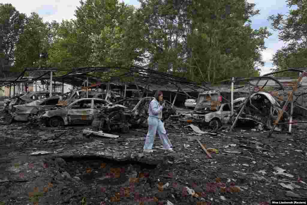 Жителька Одеси проходить повз вирву, що утворилася після удару російського безпілотника в житловому районі міста, позаду знищені автівки, 25 травня 2025 року