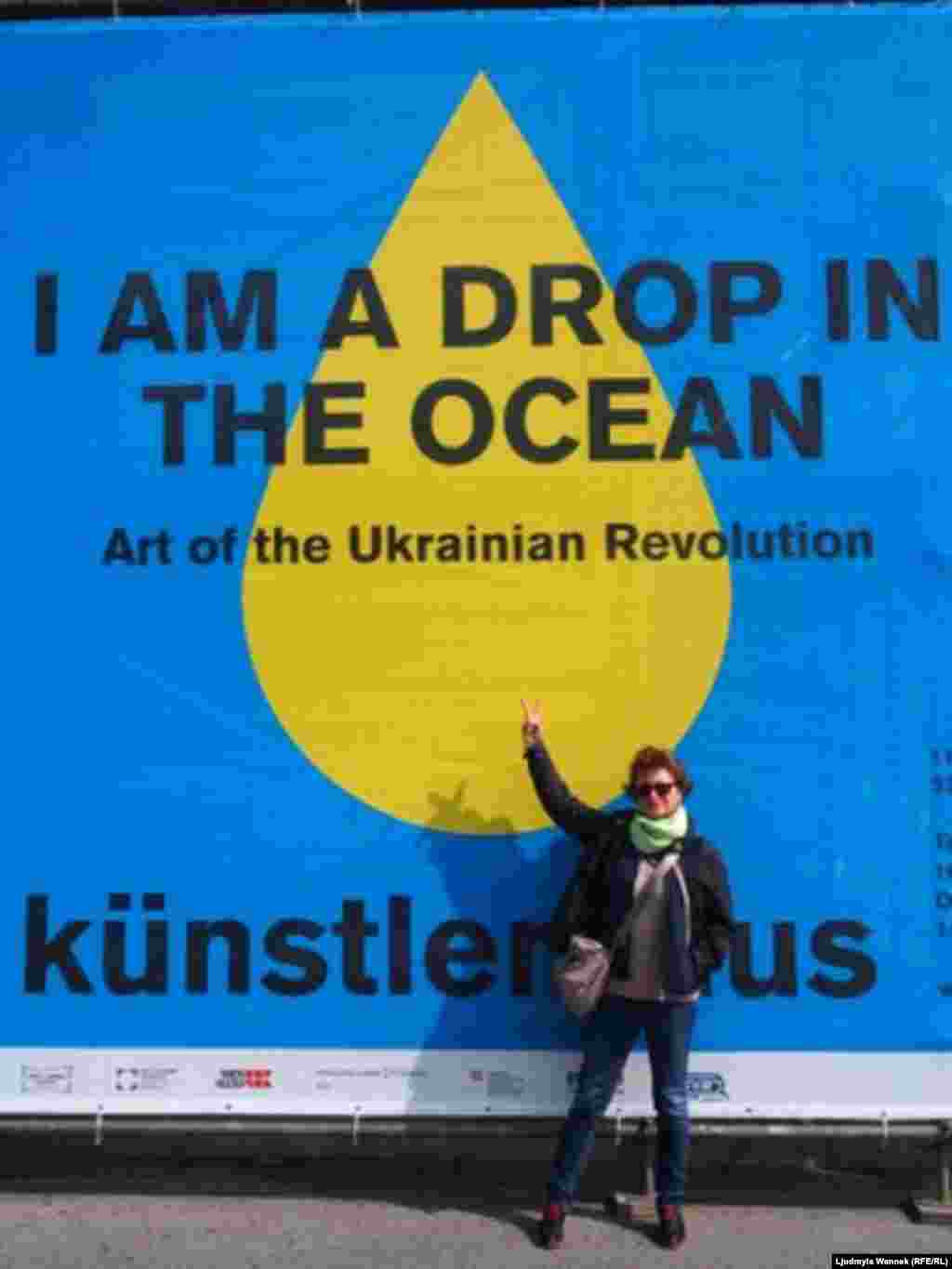 Автор фотогалереи на фоне плаката, рекламирующего выставку  