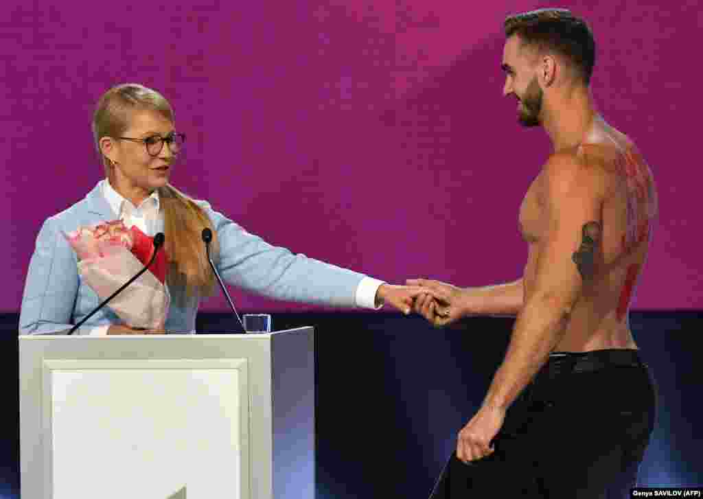 Юлія Тимошенко і чоловік, який, дякуючи їй, зняв футболку, під котрою на спині був напис «Новий курс» і символічна стрілка вниз до тієї частини тіла, що лишилася закрита штанами. Згодом чоловік сказав журналістам, що це була спланована провокація. Київ, 15 червня 2018 року