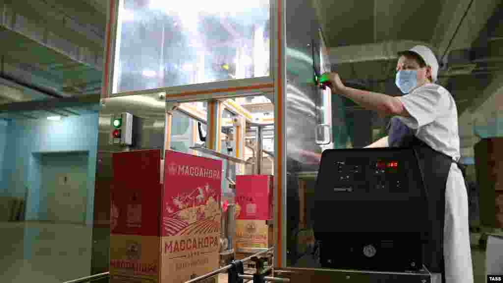 Оператор конвейера контролирует процесс упаковки бутылок вина 