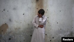 A young man stands weeping near a wall damaged by shrapnel from a bomb attack in Peshawar in January.
