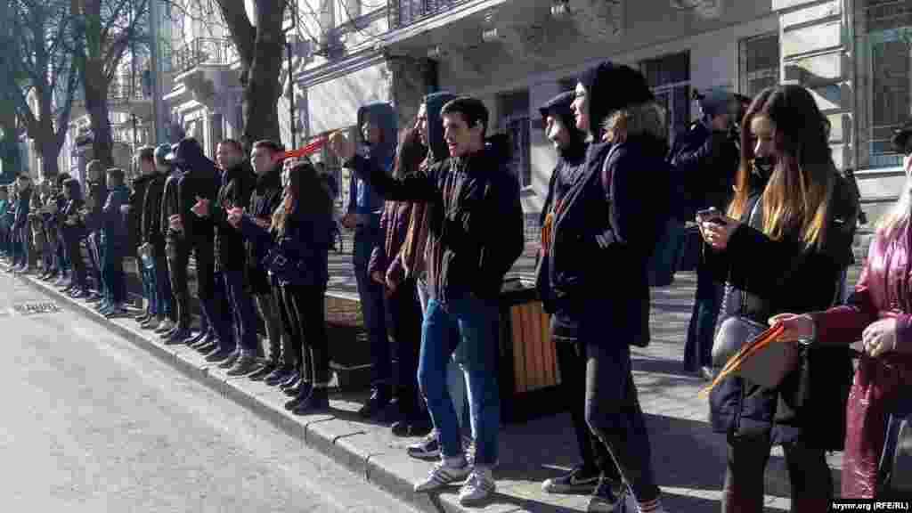 Школьники с российскими флажками и «георгиевскими ленточками» приветствуют колонну участников торжественного митинга 