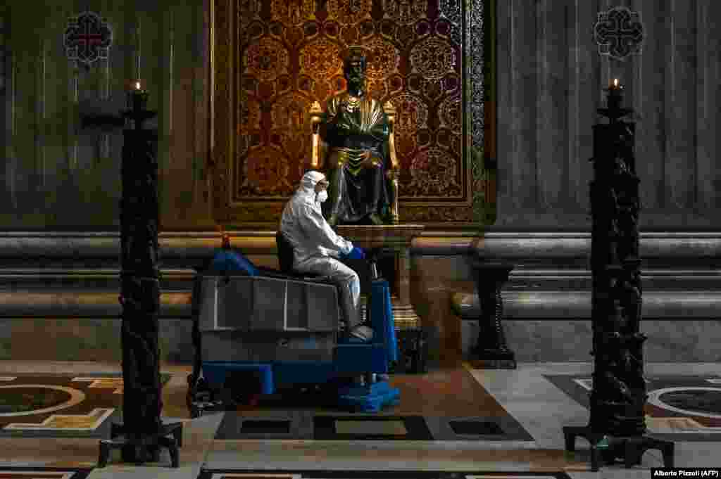 Чоловік, одягнений у захисний комбінезон та маску, проїжджає на машині для миття підлоги повз статую Святого Петра під час санітарної обробки базиліки Святого Петра у Ватикані 15 травня. (AFP/Alberto Pizzoli)
