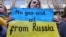 Žena na protestu u Briselu ispred nemačke ambasade drži transparent tokom demonstracija podrške Ukrajini, 11. mart 2022.