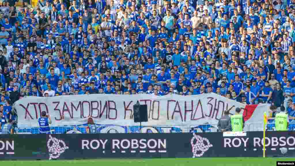 Напис на полотні «Хто замовив Катю Гандзюк?», яке розгорнули фанати команди «Динамо» під час футбольного матчу української Прем'єр-ліги. Київ, 3 серпня 2018 року