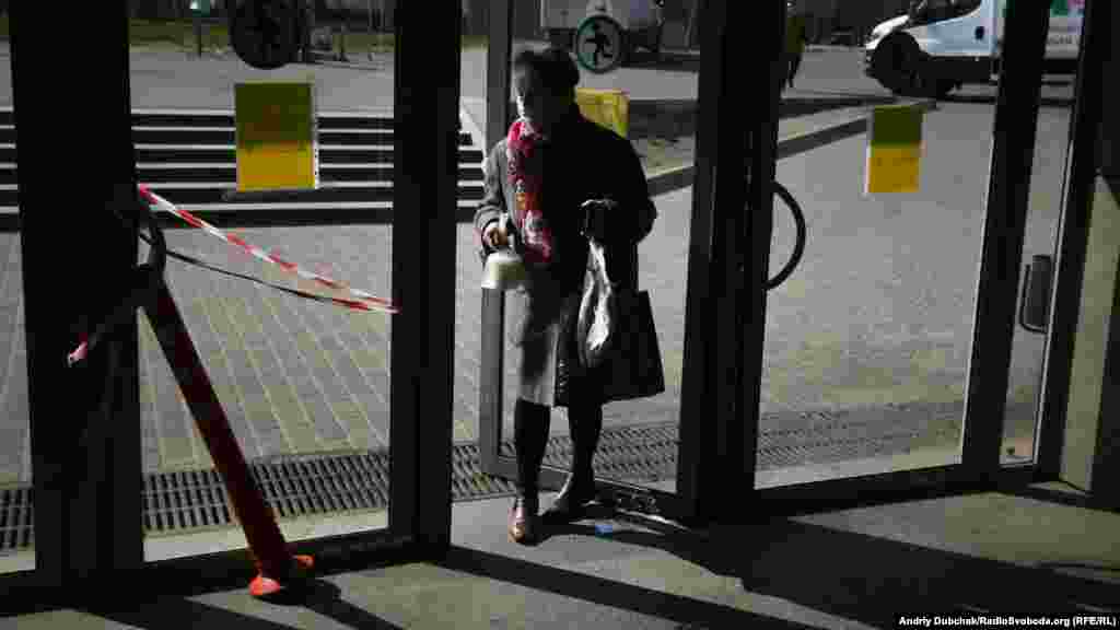 Літня жінка відчиняє спиною двері у підземному переході біля станції метро Героїв Дніпра. Коронавірус активно переноситься контактним способом, тому люди намагаються відчиняти непристосовані до цього двері в різний спосіб – ногами, ліктями, спиною 