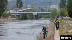 Radnici kose travu pored reke Ibar, blizu glavnog mosta u etnički podeljenoj Mitrovici, 9. septembar 2024. 