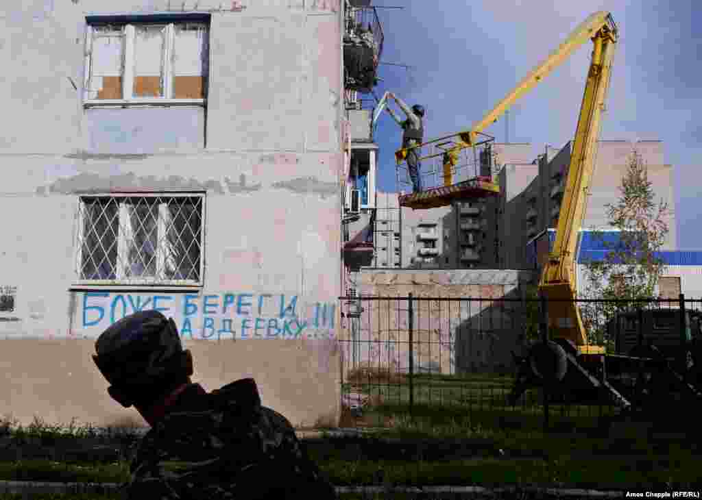 Пока ван Хелтен поднимается на рабочее место, украинский военный проходит мимо граффити: «Боже, береги Авдеевку»