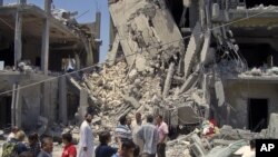 Members of the media and others examine the remains of a damaged residential building in Tripoli on June 19, 2011