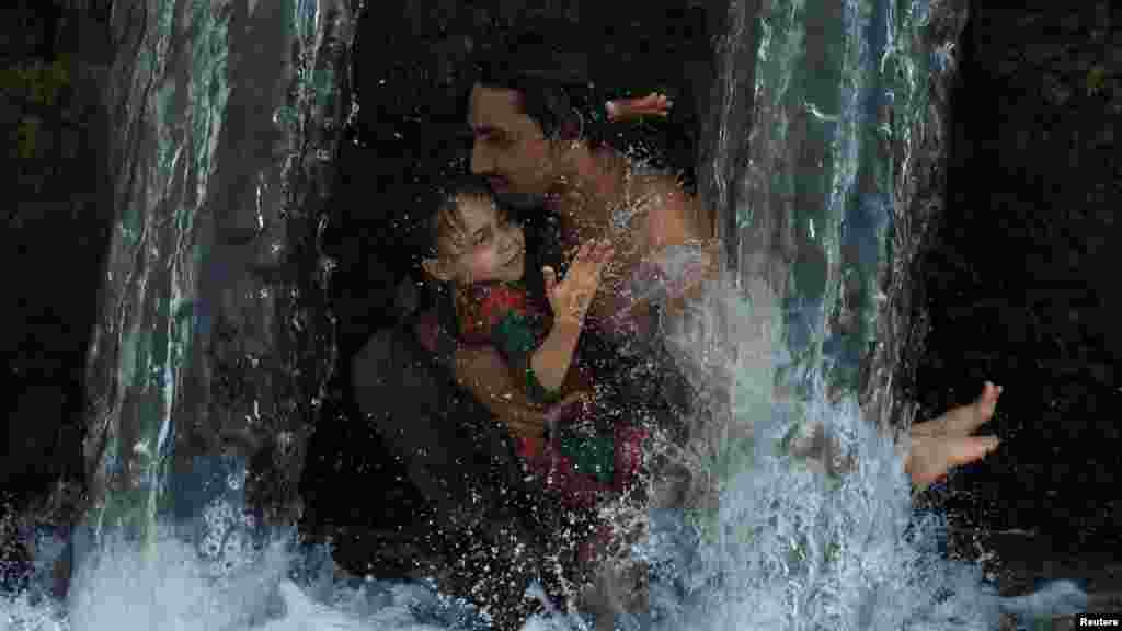 Muškarac i dete se rashlađuju vodom iz kanala u Pešavaru, Pakistan.