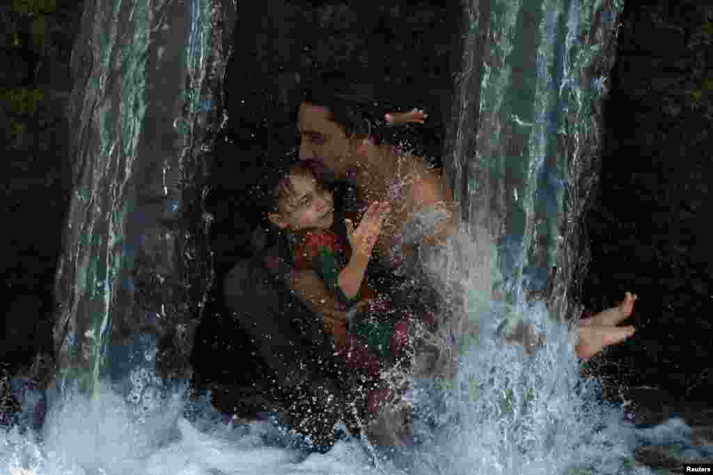 Мужчина и ребенок охлаждаются водой из канала в жаркий день, Пешавар, Пакистан, 24 июня 2025 г. REUTERS/Fayaz Aziz