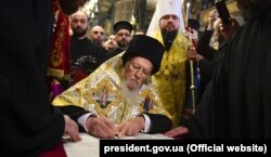 Вселенський патріарх Варфоломій підписує Томос про автокефалію для Православної церкви України (ПЦУ). По ліву руку від нього стоїть митрополит Київський і всієї України Епіфаній. Стамбул, 5 січня 2019 року