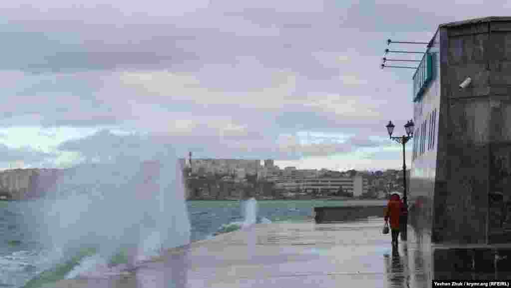 Женщина пытается проскочить между волнами возле здания «Аквариума»