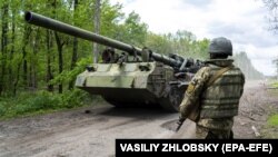 يو اوکراينی پوځي د هغه ټينک سره ولاړ دی چې د جګړې لومړۍ کرښې ته ځي. (انځور له ارشيفه)